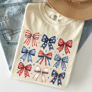 Comfort Colors patriotic bow shirt featuring red white and blue coquette bows for Fourth of July celebrations