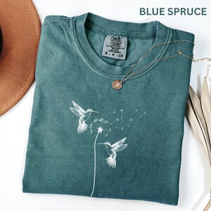 a green t-shirt with a white bird design, a brown hat, and a necklace with a pendant, all placed on a white surface.