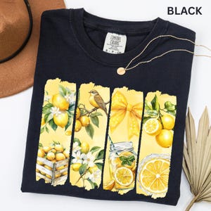May include: Black t-shirt with a vibrant yellow and white lemon-themed graphic. The design includes lemons, a bird, a bow, and a mason jar with a lemon slice. The word "BLACK" is printed at the top.