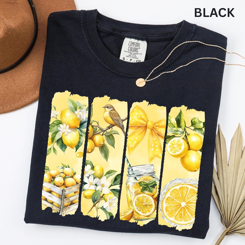 May include: Black t-shirt with a vibrant yellow and white lemon-themed graphic. The design includes lemons, a bird, a bow, and a mason jar with a lemon slice. The word "BLACK" is printed at the top.