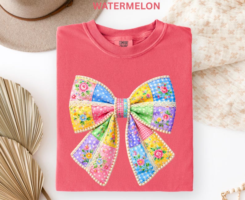 May include: A coral-coloured t-shirt with a large patchwork bow design. The bow features various patterns, including floral prints, polka dots, and gingham, in shades of pink, blue, yellow, and green. The word "WATERMELON" is printed at the top.