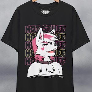Puede incluir: Camiseta negra con una criatura peluda blanca con pelo rosa y un corazón rosa en la mejilla. La criatura lleva un collar negro. El texto "HOT STUFF" se repite en rosa y amarillo en la camiseta.