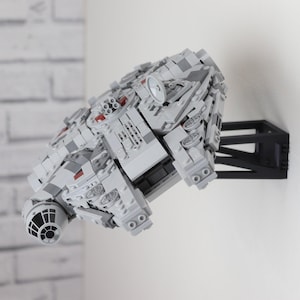 Può includere: Un modello Lego del Millennium Falcon bianco e grigio montato su un supporto da parete nero. Il modello è dettagliato con accenti rossi e presenta una cabina di pilotaggio e un motore dettagliati.