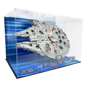 Könnte beinhalten: Ein detailliertes Modell des Raumschiffs Millennium Falcon, aus ineinandergreifenden Kunststoffbausteinen, ausgestellt in einem transparenten Acrylgehäuse. Das Modell ist grau mit roten und schwarzen Akzenten, vor blauem Hintergrund.