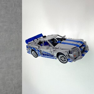 Könnte beinhalten: Ein silber-blaues Modellauto mit Spoiler. Das Auto hat blaue Streifen und Akzente und ist eine detaillierte Nachbildung eines Sportwagens. Das Modell ist aus Kunststoff und weist sichtbare mechanische Details auf.