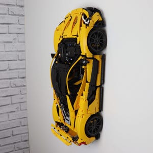 May include: A yellow and black model sports car mounted on a white wall. The car features black wheels and intricate detailing, showcasing its design. The model is a replica of a high-performance vehicle.