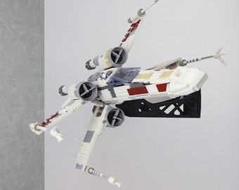 May include: A white and red X-wing starfighter model with four engines and detailed wings. The model is mounted on a black display stand, showcasing its design. The model is a replica of the iconic Star Wars spacecraft.