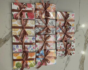 May include: A collection of gift boxes wrapped in patterned paper and tied with brown satin ribbons. The boxes feature various designs, including fruits, flowers, and bicycles. The ribbons are tied in a bow.