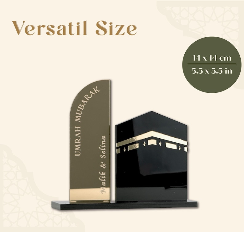 Op de afbeelding: Een decoratieve zwarte en gouden Umrah Mubarak display. De display heeft een gestileerde Kaaba en een verticale plaat met de tekst "UMRAH MUBARAK" en "Malik & Selina". Afmetingen: 14 x 14 cm.