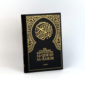 Könnte beinhalten: Ein schwarzes Buch mit goldenen Lettern und einem dekorativen Rand. Der Titel lautet "DIE UNGEFÄHRE BEDEUTUNG DES AL-QUR'AN AL-KARIM" und der Autor ist "RAUDA".