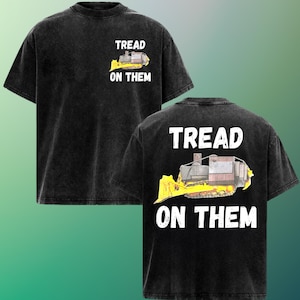 May include: Black t-shirt with a distressed look. The front features a graphic of a yellow and brown bulldozer with the text "TREAD ON THEM." The same design is repeated on the back of the shirt.