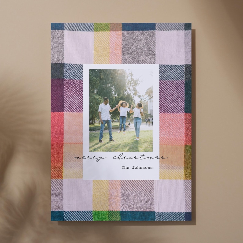 May include: A Christmas card with a plaid background and a photo of a family of three. The text "merry christmas" and "The Johnsons" is printed on the card.