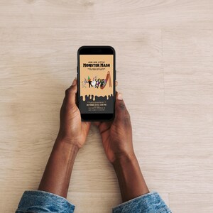 Hands holding a smartphone that displays a digital Monster Mash party invitation on a light wooden table background.