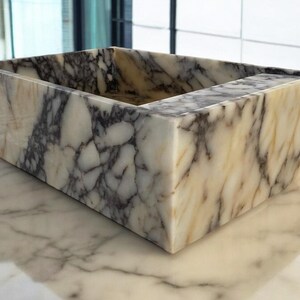 May include: A rectangular marble sink with a white, grey, and brown marbled pattern. The sink is made of natural stone and has a smooth, polished finish.