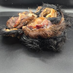 May include: Close-up of several dried animal ears with fur. The ears are a mix of brown, black, and tan colors, with visible textures and details. The image is taken against a dark background.
