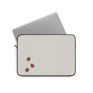 Może przedstawiać: Prostokątne etui na laptopa z jasnobeżowym tłem i wzorem w małe czarne kropki. Trzy czerwone biedronki w czarne kropki znajdują się w lewym dolnym rogu etui. Etui posiada czarne wykończenie z zamkiem błyskawicznym.