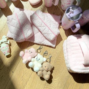 May include: Three plush teddy bears with keychains, a pink quilted makeup bag, two pink quilted zippered pouches, and a pink and silver tumbler with a straw.