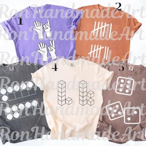 May include: Five different t-shirts, each with a unique graphic. Designs include hand gestures, tally marks, a counting frame, geometric shapes, and dice. The shirts are in various colors: purple, orange, gray, cream, and brown.