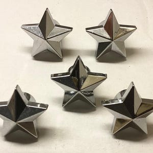 May include: Five silver star-shaped metal decorative pieces. Each star has five points and a raised center.