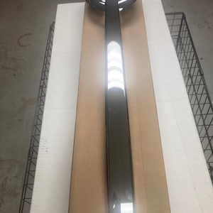 May include: A chrome-finished automotive part, likely a bumper or trim piece, is displayed on a cardboard surface. The part has a rounded, bowl-like end and a long, rectangular body. The reflective surface suggests a polished metal finish.