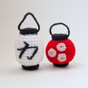 May include: Two crocheted lanterns, one white with a black kanji character and one red with pink polka dots.