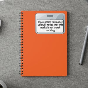 May include: An orange spiral-bound notebook with a white rectangle containing the text: "If you notice this notice you will notice that this notice is not worth noticing." A silver pen is on the surface.