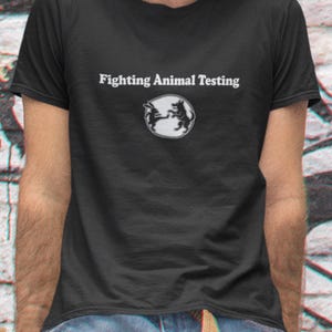 May include: Black t-shirt with the text "Fighting Animal Testing" above a circular graphic of two animals. The shirt is short-sleeved and made of a dark fabric. The person is wearing blue jeans.