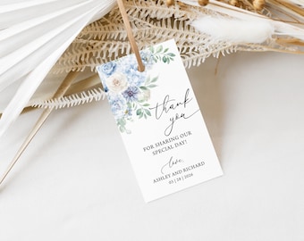 Può includere: Un'etichetta bianca con un design floreale con fiori blu e crema e foglie verdi. L'etichetta recita "thank you" in una scrittura elegante, con il testo "FOR SHARING OUR SPECIAL DAY!" e i nomi "ASHLEY AND RICHARD" e la data.