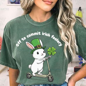 May include: Green t-shirt with the text "off to commit irish foolery". The shirt features a white cartoon rabbit wearing a green hat and holding a four-leaf clover while riding a scooter.