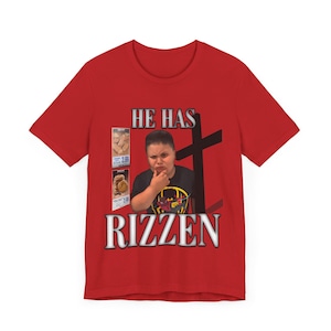 Op de afbeelding: Rood T-shirt met een witte afbeelding met de tekst "He Has Rizzn" met een afbeelding van een jonge jongen met een kruis erachter. De afbeelding bevat ook een afbeelding van een doos met snacks.