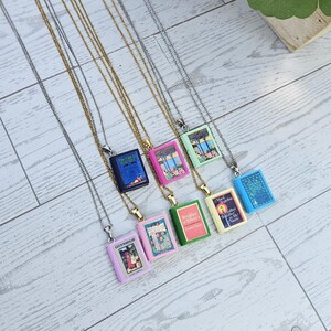 May include: A collection of seven necklaces featuring miniature book pendants with colourful covers. The pendants include titles such as The Great Gatsby, Alice in Wonderland, and Breakfast at Tiffany's, suspended on thin silver and gold-toned metal chains.