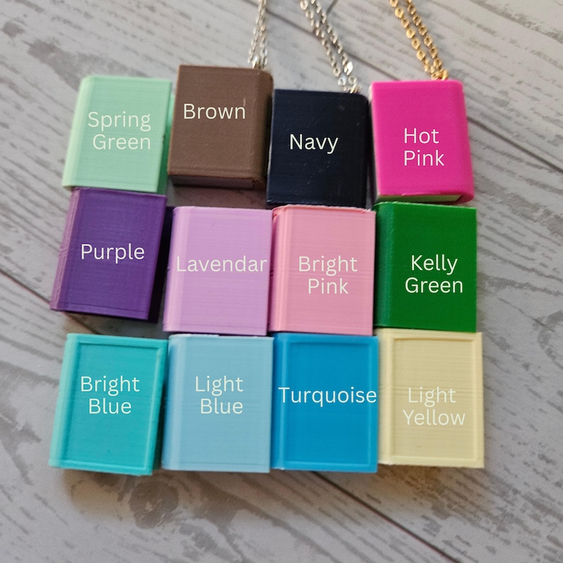 Op de afbeelding: Een verzameling van twaalf rechthoekige, boekvormige hangers aan metalen kettingen, elk gelabeld met de kleur: Spring Green, Brown, Navy, Hot Pink, Purple, Lavendar, Bright Pink, Kelly Green, Bright Blue, Light Blue, Turquoise en Light Yellow.