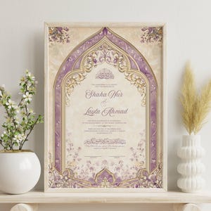 May include: Framed wedding certificate with a beige and purple floral design. The certificate features the names "Shaha Nur & Layla Ahmad" in elegant script. The frame is a light wood color, and the overall aesthetic is ornate and decorative.