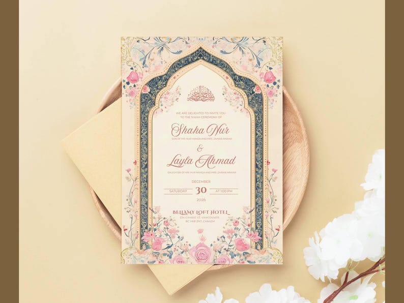 May include: An invitation card with floral and ornamental design. The card features the names "Shaha Nur" and "Layla Ahmad" with the date "December 30". The card is placed on a wooden plate with a cream-colored envelope.