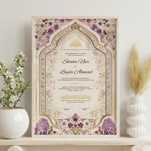 May include: Framed wedding certificate with ornate floral and geometric designs in cream, gold, and purple. The names "Shaha Nur" and "Layla Ahmad" are displayed. A white vase with flowers and a white vase with dried plants are on either side.
