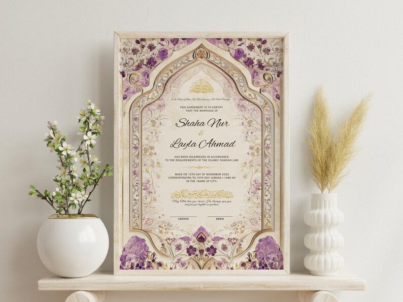 May include: Framed wedding certificate with ornate floral and geometric designs in cream, gold, and purple. The names "Shaha Nur" and "Layla Ahmad" are displayed. A white vase with flowers and a white vase with dried plants are on either side.