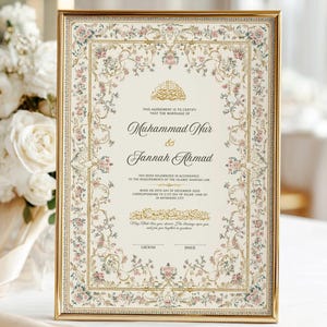 May include: A rectangular gold-framed marriage certificate featuring a cream-colored background with an intricate floral border in shades of pink, blue, and green. The text includes the names Muhammad Nur and Jannah Ahmad with Islamic calligraphy.