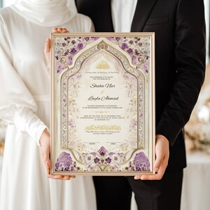 May include: A framed wedding certificate with a gold border. The certificate features ornate floral designs in purple and gold, with the names "Shaha Nur" and "Layla Ahmad" prominently displayed. The couple is holding the framed certificate.