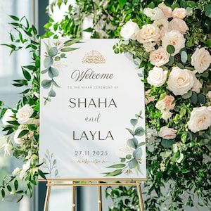 Op de afbeelding: Een welkomstbord voor een Nikah-ceremonie met de namen Shaha en Layla, gedateerd 27.11.2025. Het bord staat op een gouden ezel en is omgeven door witte rozen, groen en eucalyptusbladeren. De tekst "Welcome to the Nikah Ceremony" is zichtbaar.
