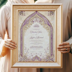 May include: Framed wedding invitation with a gold border, featuring a central design in shades of purple and cream. The invitation includes the names "Shaha Hur & Layla Ahmad" in elegant script, with decorative floral elements.