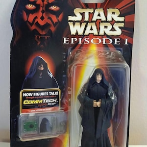 May include: A Star Wars Episode I Darth Sidious action figure in a sealed package. The packaging features Darth Maul's face and the Star Wars logo. The figure is wearing a black robe. The package includes a CommTech chip.