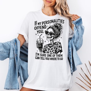 K&ouml;nnte beinhalten: Wei&szlig;es T-Shirt mit einem schwarzen Aufdruck eines Skeletts mit Sonnenbrille und einem Getr&auml;nk. Der Text lautet: &bdquo;WENN MEINE PERS&Ouml;NLICHKEITEN DICH BELEIDIGEN, BIN ICH SICHER, DASS EINE VON IHNEN DIR SAGEN KANN, WO ES HIN GEHT.&ldquo;