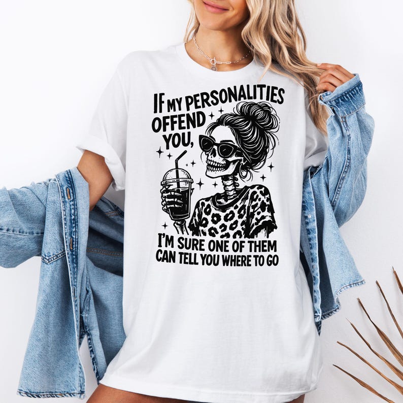 K&ouml;nnte beinhalten: Wei&szlig;es T-Shirt mit einem schwarzen Aufdruck eines Skeletts mit Sonnenbrille und einem Getr&auml;nk. Der Text lautet: &bdquo;WENN MEINE PERS&Ouml;NLICHKEITEN DICH BELEIDIGEN, BIN ICH SICHER, DASS EINE VON IHNEN DIR SAGEN KANN, WO ES HIN GEHT.&ldquo;
