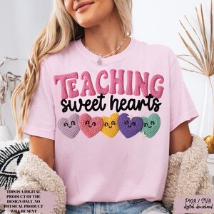 May include: A light pink t-shirt with the words "TEACHING sweet hearts" in pink and black. Below the text are five colorful heart-shaped designs. The shirt is a digital product.