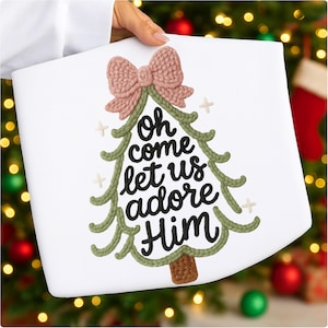 Puede incluir: Bolso tote blanco con diseño de árbol de Navidad tejido, lazo rosa y la frase "Oh come let us adore Him" en escritura negra. El árbol está delineado en verde con acentos de cruz blancos.