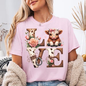 Pu&ograve; includere: T-shirt rosa chiaro con la scritta "LOVE" in un design rustico. La "L" e la "E" sono in legno, la "O" ha un motivo a pelle di mucca e la "V" un ferro di cavallo. Un simpatico vitello con un fiocco rosa &egrave; sopra la "E".
