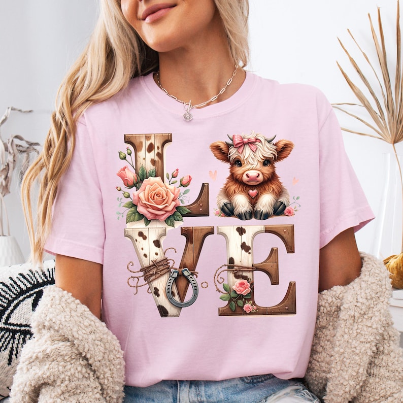 Pu&ograve; includere: T-shirt rosa chiaro con la scritta "LOVE" in un design rustico. La "L" e la "E" sono in legno, la "O" ha un motivo a pelle di mucca e la "V" un ferro di cavallo. Un simpatico vitello con un fiocco rosa &egrave; sopra la "E".