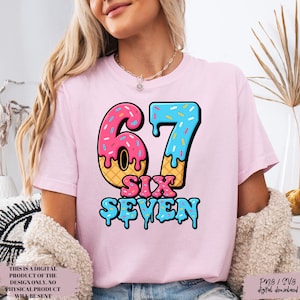 May include: A light pink t-shirt with a colorful graphic of the number "67" in a donut-style design. The words "SIX SEVEN" are below the number. The shirt also has text that reads "THIS IS A DIGITAL PRODUCT OF THE DESIGN ONLY. NO PHYSICAL PRODUCT WILL BE SENT" and "Png / SVS digital download".