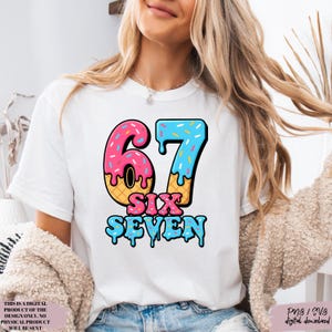 May include: White t-shirt featuring a colorful graphic of the number "67" designed to look like ice cream cones, with the words "SIX SEVEN" below. The design includes pink, blue, and yellow colors. The shirt is a digital product.
