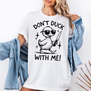 May include: White t-shirt with a black graphic of a duck wearing sunglasses and holding a knife. The text "DON'T DUCK WITH ME!" is above and below the duck illustration.